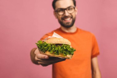 Hamburger tutan genç bir adam. Öğrenci fast food yiyor. Burger yararlı bir yemek değildir. Çok aç bir adam. Diyet konsepti. Pembe arka planda izole edilmiş.