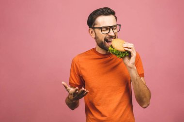 Hamburger tutan genç bir adam. Öğrenci fast food yiyor. Burger yararlı bir yemek değildir. Çok aç bir adam. Diyet konsepti. Pembe arka planda izole edilmiş.