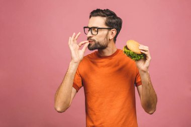 Hamburger tutan genç bir adam. Öğrenci fast food yiyor. Burger yararlı bir yemek değildir. Çok aç bir adam. Diyet konsepti. Pembe arka planda izole edilmiş.