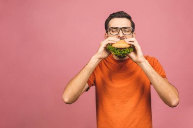 Hamburger tutan genç bir adam. Öğrenci fast food yiyor. Burger yararlı bir yemek değildir. Çok aç bir adam. Diyet konsepti. Pembe arka planda izole edilmiş.