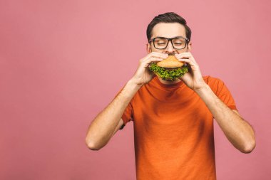 Hamburger tutan genç bir adam. Öğrenci fast food yiyor. Burger yararlı bir yemek değildir. Çok aç bir adam. Diyet konsepti. Pembe arka planda izole edilmiş.