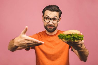 Hamburger tutan genç bir adam. Öğrenci fast food yiyor. Burger yararlı bir yemek değildir. Çok aç bir adam. Diyet konsepti. Pembe arka planda izole edilmiş.