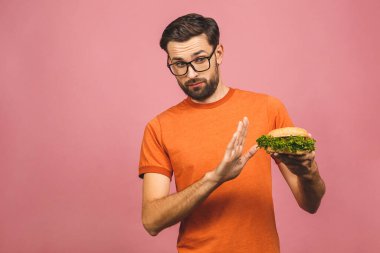 Sağlıksız hamburgeri reddeden yakışıklı genç adam pembe arka planda izole edilmiş. Diyet konsepti. Metin için kopyalama alanı ile.