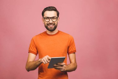 Sıradan ayakta duran ve pembe arka planda izole edilmiş tablet kullanan mutlu genç adam..