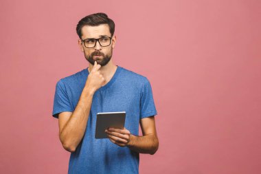 Sıradan ayakta duran ve pembe arka planda izole edilmiş tablet kullanan mutlu genç adam..