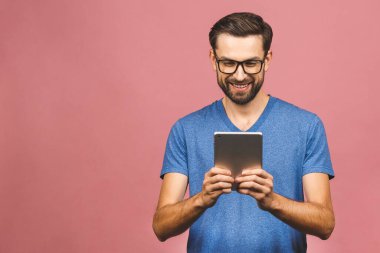 Sıradan ayakta duran ve pembe arka planda izole edilmiş tablet kullanan mutlu genç adam..