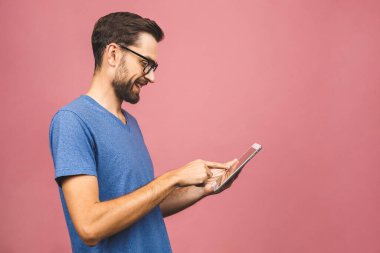 Sıradan ayakta duran ve pembe arka planda izole edilmiş tablet kullanan mutlu genç adam..
