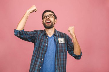 Kareli gömlekli genç adam cebinde dolar banknotları tutuyor ve sürpriz bir şekilde pembe arka planda izole edilmiş.. 