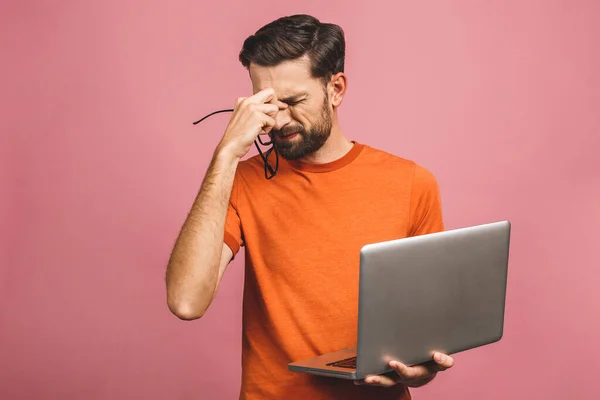 Pembe arka planda dizüstü bilgisayar tutan dalgın üzgün genç adam..