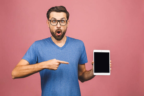 Bearded amazed man in eyeglasses which showing blank tablet computer screen and looking at camera. Isolated over pink background. 