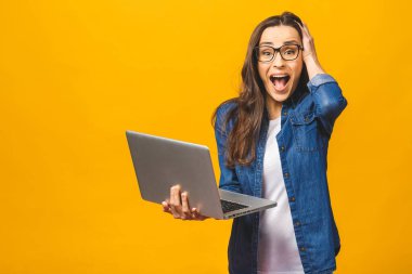 Aman Tanrım! Şok oldum! Sarı arka planda dizüstü bilgisayar tutan şok olmuş güzel bir kızın portresi..