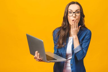 Aman Tanrım! Şok oldum! Sarı arka planda dizüstü bilgisayar tutan şok olmuş güzel bir kızın portresi..