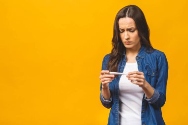 Bacası olan genç bir kadın termometre alıyor. Sarı arka planda izole edilmiş. Güzel genç bir kadın yüksek sıcaklıkta, termometrede ve izole edilmiş yakın çekimlerde hasta. Soğuk, grip konsepti.