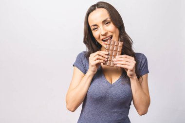 Çikolata yiyip gülümseyen genç ve mutlu bir bayan. Tatlı çikolatanın tadına bakan bir kız. Doğal makyajlı genç bir kadın beyaz arka planda izole edilmiş çikolata yiyip eğleniyor.