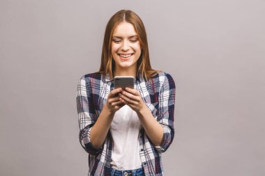 Gri duvar arkasında izole edilmiş, cep telefonuyla sohbet eden neşeli, hoş, genç bir kadının fotoğrafı..