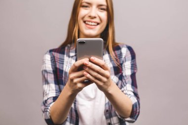 Gri duvar arkasında izole edilmiş, cep telefonuyla sohbet eden neşeli, hoş, genç bir kadının fotoğrafı..