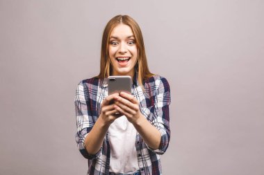 Gri duvar arkasında izole edilmiş, cep telefonuyla sohbet eden neşeli, hoş, genç bir kadının fotoğrafı..