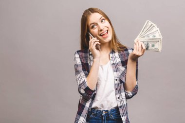 Mutlu, heyecanlı bir kadının portresi. Gri arka planda izole edilmiş bir sürü para banknotunu tutarken cep telefonuyla konuşuyor..