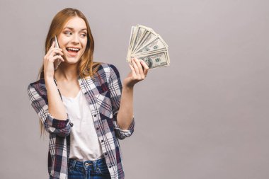 Mutlu, heyecanlı bir kadının portresi. Gri arka planda izole edilmiş bir sürü para banknotunu tutarken cep telefonuyla konuşuyor..