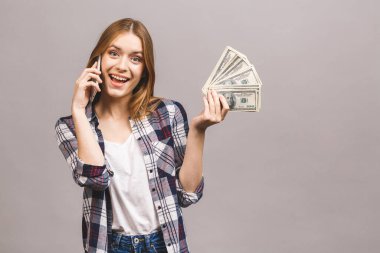 Mutlu, heyecanlı bir kadının portresi. Gri arka planda izole edilmiş bir sürü para banknotunu tutarken cep telefonuyla konuşuyor..