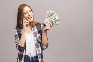 Mutlu, heyecanlı bir kadının portresi. Gri arka planda izole edilmiş bir sürü para banknotunu tutarken cep telefonuyla konuşuyor..