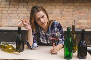 Mutfaktaki kanepede oturan, sarhoş sarhoş kırmızı şarap içen, üzgün, alkolik ve akşamdan kalma genç ve sarhoş bir kadın..