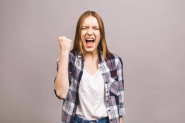 Happy winner! Close-up of emotional young attractive woman with keeping hands in fists, isolated on grey background. Surprised young woman shouting.