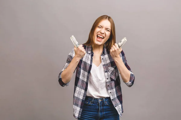 Happy winner! Portrait of a playful young woman with long hair holding bunch of money banknotes and looking at camera, copy space, isolated over grey background.