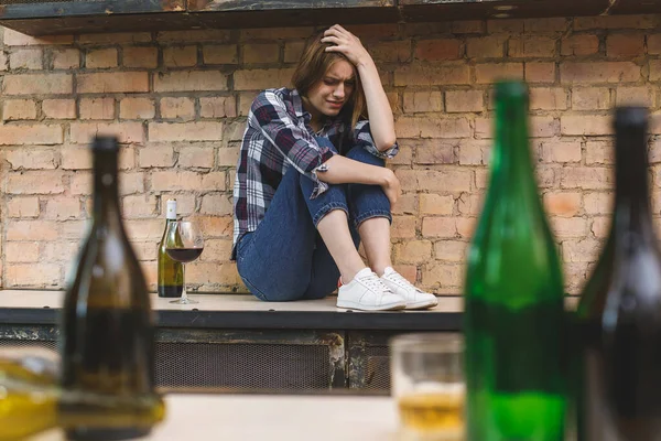 Young woman alcoholic social problems concept sitting with closed eyes in kitchen. Depression young female teenager having abused problem feeling suffering and crying.