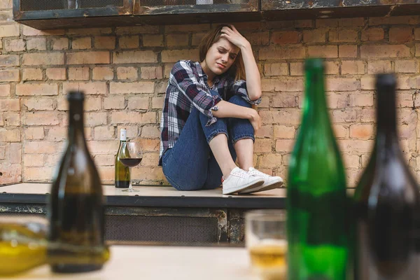 Young woman alcoholic social problems concept sitting with closed eyes in kitchen. Depression young female teenager having abused problem feeling suffering and crying.