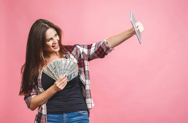 お金を持っている陽気な若い女性の肖像銀行券とピンクの背景に隔離されたお祝い タブレットを使う — ストック写真