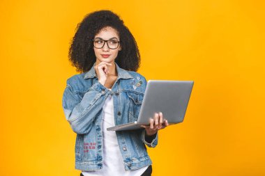 Genç Afro-Amerikan siyah, kıvırcık saçlı, dizüstü bilgisayar kullanan ve sarı arka planda sırıtan havalı bayan.. 