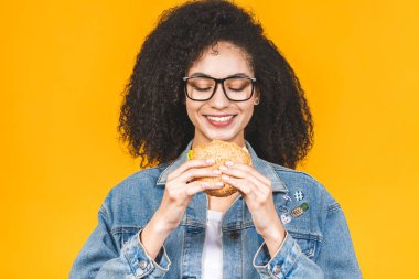 Sarı arka planda izole edilmiş hamburger yiyen Afro-Amerikalı genç kadın..