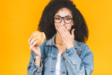 Sarı arka planda izole edilmiş hamburger yiyen Afro-Amerikalı genç kadın..