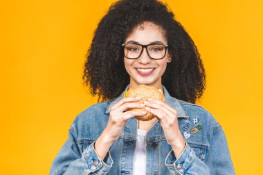 Sarı arka planda izole edilmiş hamburger yiyen Afro-Amerikalı genç kadın..