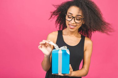 Mutlu Afro-Amerikan kıvırcık bayanı pembe arka planda izole edilmiş hediyesini tutarken gülerken.