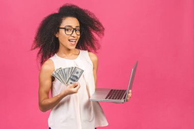 Mutlu galip. Afro-Amerikan 20 'li yaşlarda başarılı bir kadının portresi. Elinde bir sürü para banknotları ve pembe arka planda izole edilmiş dizüstü bilgisayar var..