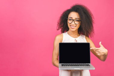 Kıvırcık saçlı genç Afrikalı bir bayan pembe arka planda boş ekranlı dizüstü bilgisayar gösteriyor.. 