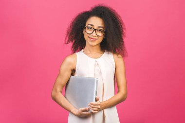 Genç Afro-Amerikalı siyah, kıvırcık saçlı, dizüstü bilgisayarı olan ve pembe arka planda sırıtan havalı bir bayan.. 