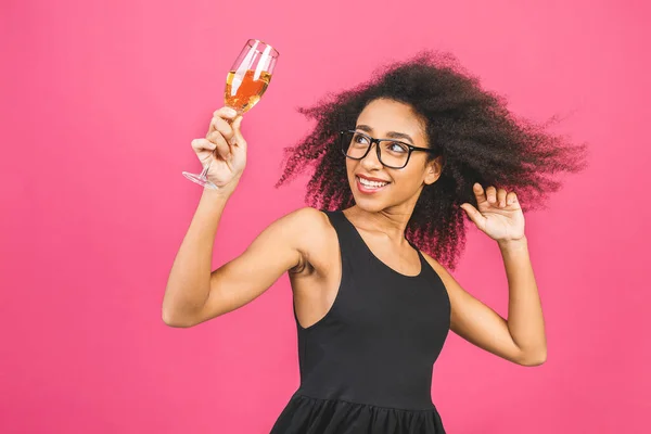 Happy birthday! Portrait of happy African-American black woman with glass of champagne isolated over pink background.