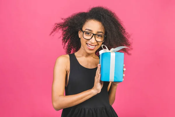 Happy african american curly lady in casual laughing while holding present isolated over pink background.