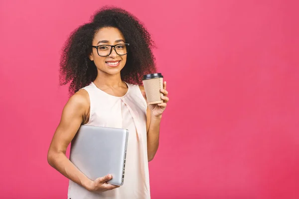 Young african american black positive cool lady with curly hair holding laptop and smiling isolated over pink background. Drinking cup of tea or coffee.