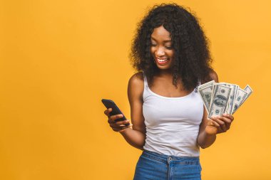 Mutlu galip. Afro saçlı, 20 'li yaşlarda, elinde bir sürü para banknotları olan ve sarı arka planda izole edilmiş telefon kullanan Afrikalı Amerikalı başarılı bir kadının portresi..