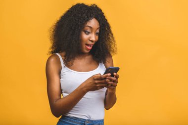 Onun portresi güzel, güzel, çekici, çekici, mutlu, mutlu, neşeli, dalgalı saçlı, Afro-Amerikalı siyah kız el ele tutuşmuş, telefon görüşmeleri yapıyor sarı arka planda izole bir şekilde..