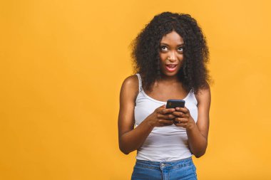 Onun portresi güzel, güzel, çekici, çekici, mutlu, mutlu, neşeli, dalgalı saçlı, Afro-Amerikalı siyah kız el ele tutuşmuş, telefon görüşmeleri yapıyor sarı arka planda izole bir şekilde..