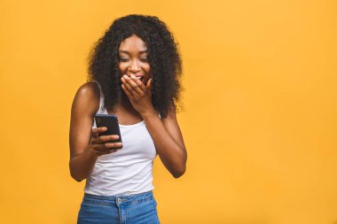 Onun portresi güzel, güzel, çekici, çekici, mutlu, mutlu, neşeli, dalgalı saçlı, Afro-Amerikalı siyah kız el ele tutuşmuş, telefon görüşmeleri yapıyor sarı arka planda izole bir şekilde..