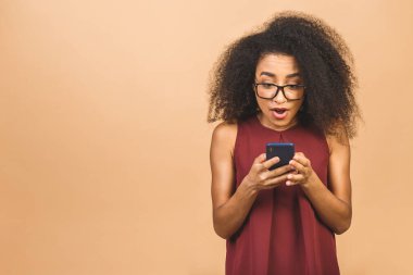 Onun portresi, güzel, güzel, çekici, güzel, çekici, mutlu, neşeli, dalgalı saçlı, Afro-Amerikalı siyah kız. El ele tutuşmuş, telefonda, bej arka planda izole edilmiş internette sohbet ediyor..
