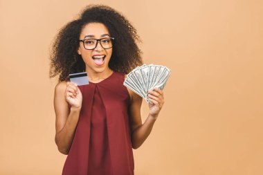 Mutlu galip. Afro saç stili olan 20 'li yaşlardaki Afrikalı Amerikalı başarılı kadının portresi bir sürü para banknotu ve bej arka planda izole edilmiş kredi kartı taşıyor.. 