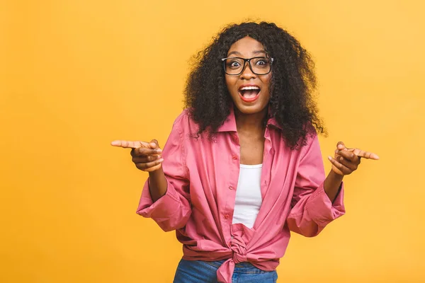 Portrait of cheerful young african american woman with curly hair posing in studio with happy smile. Dark-skinned woman smiling joyfully. Isolated over yellow background.