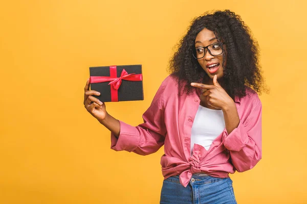 Happy african american lady in casual looking aside and laughing while holding present isolated over yellow background.